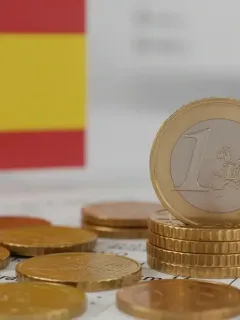 Monedas de euro españolas apiladas sobre documentos oficiales, simbolizando el ahorro gubernamental y los beneficios financieros en España.