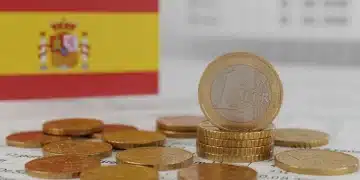 Monedas de euro españolas apiladas sobre documentos oficiales, simbolizando el ahorro gubernamental y los beneficios financieros en España.
