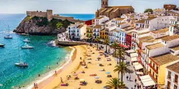 Vista panorámica de una playa española con turistas y arquitectura histórica, reflejando el dinamismo del turismo en España.