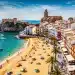 Vista panorámica de una playa española con turistas y arquitectura histórica, reflejando el dinamismo del turismo en España.